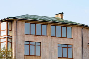 Metal roofing. Large modern house with large windows and balconies. Rain gutter on the roof top of house. metal roof. Chimney pipe.