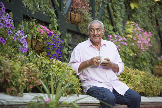 Hispanic man drinking coffee in flower garden