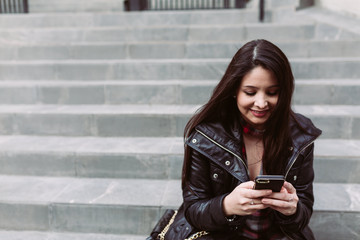Junge Frau lächelt mit Handy auf Treppe / Straße