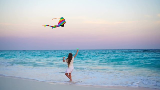 Adorable little girl with flying kite on tropical beach at sunset. Kids play on ocean shore. Child with beach toys.