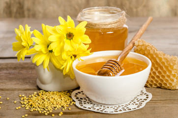 Yellow flowers and bee products (honey, pollen, honeycombs) on wooden background