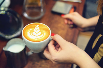 Female hand barista with a white cup of fragrant cappuccino with a beautiful