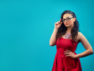 Young serious girl with makeup, wearing glasses and a red dress