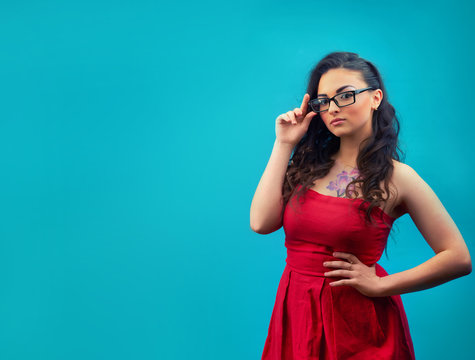 Young serious girl with makeup, wearing glasses and a red dress