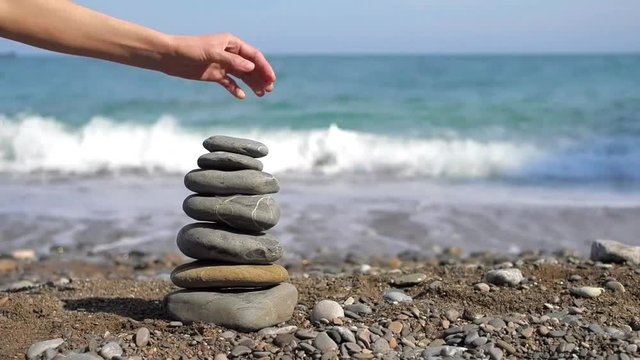 Woman's hand puts pebble in pyramid on the sea