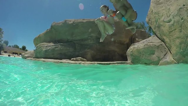 Girl and boy jumping into the water from the rock on the shore
