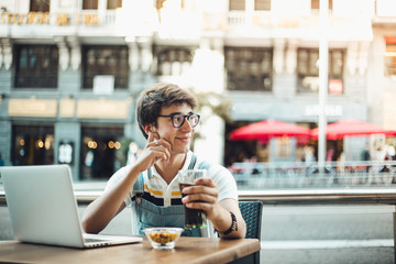 Young asian boy having a refreshment in the center of Madrid with his laptop. Young man wearing vintage clothing
