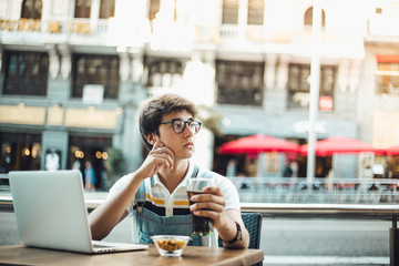 Young asian boy having a refreshment in the center of Madrid with his laptop. Young man wearing vintage clothing