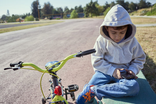 Hispanic boy sitting near bicycle texting on cell phone