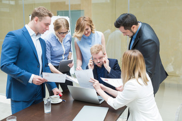 Young businessman working on laptop, around him are colleagues asking for a job