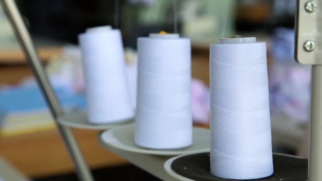 Closeup of three big bobbins with thin white thread on working professional sewing machine. Real time full hd video footage.