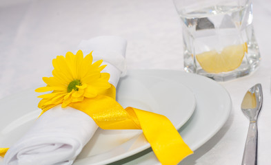 White dinning set with yellow band, flower and a glass of water with a slice of lemon