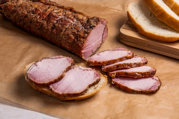 Slices smoked meat or ham on brown packing paper. Slices white wheat bread on wooden cutting board.