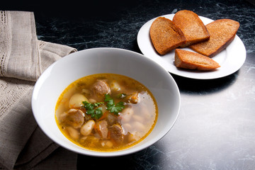 Bean soup in white plate, several toast on white plate on a black stone background.