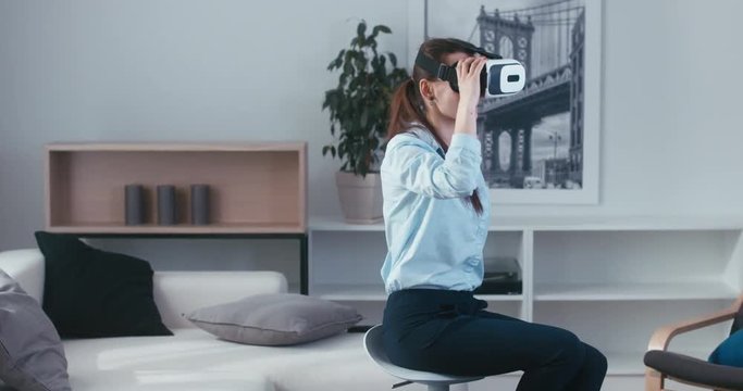 Excited Caucasian female in casual clothes using VR headset indoors, watching 360 video at home. 4K UHD RAW edited footage 