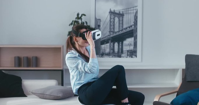 Excited Caucasian female in casual clothes using VR headset indoors, watching 360 video at home. 4K UHD RAW edited footage 