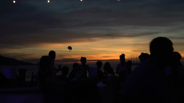 Silhouettes of people hanging out at the beach club during beautiful sunset - video in slow motion
