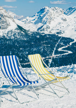 Toned image of vintage folding chairs on a piste against ski resort area in Italy