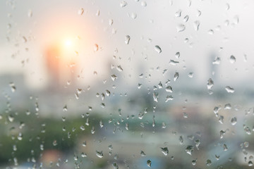 Rain drops on window glass and blurred cityscape and sunlight in background.