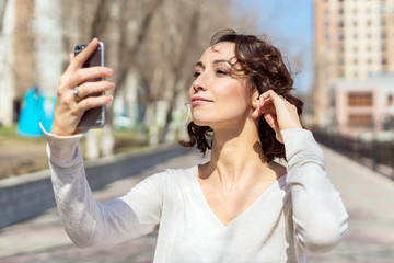 A young brunette looks in her phone, the girl uses a phone instead of a mirror and adjusts her hair