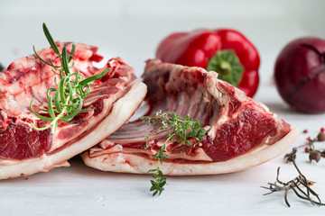 Raw red fresh saddle of mutton with herbs and vegetables on white. Closeup.