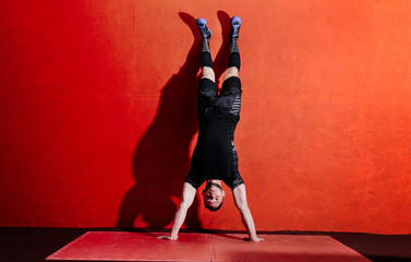 Athlete doing push ups on his hands while standing upside down near red wall. Full body length portrait