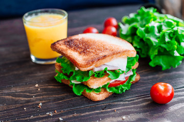 Breakfast sandwich and orange juice, tomatoes on the wooden table top view