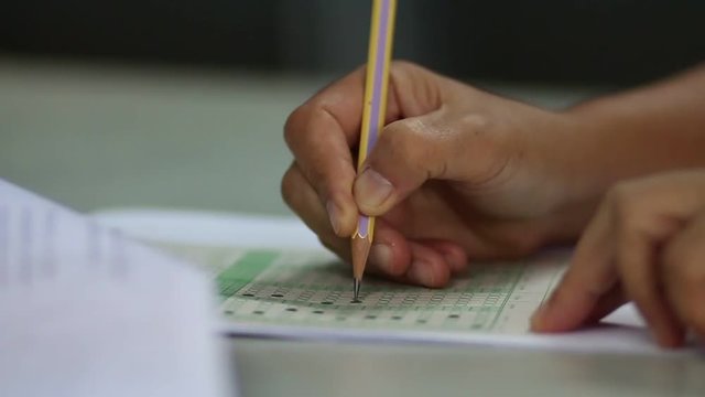 Asian students hand doing examination or exam on exercise sheet with pencil drawing selected choice on answer sheets in school exam at college