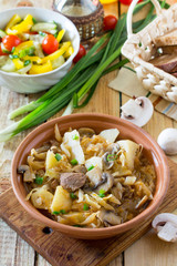 Stewed cabbage with mushrooms, mushrooms and tomato sauce with fresh vegetables on a wooden table.