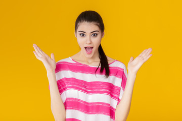 portrait of surprised young brunette woman in pink shirt on yellow background. girl looks at camera