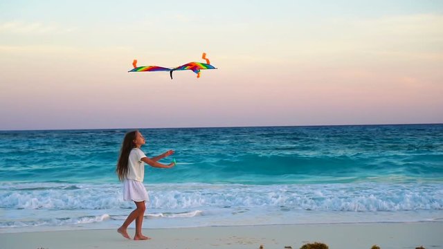 Adorable little girl with flying kite on tropical beach. Happy kid playing on ocean shore with beach kite. Slow moion