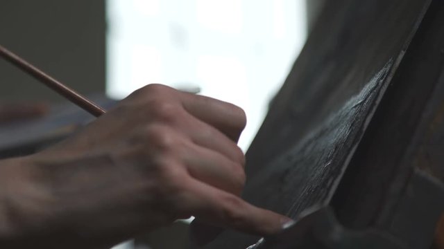 The process of drawing on canvas: unknown artist paints a fine brush on a canvas. In the shot only the hand of the artist, brush and canvas on the easel. The artist at work draws a picture