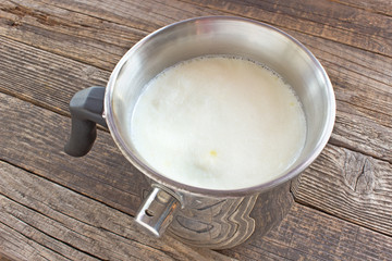 Hot milk boiled in metal pot with whistling alarm on wooden table