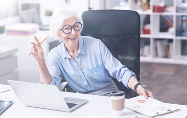 Positive delighted elderly woman sitting on office chair