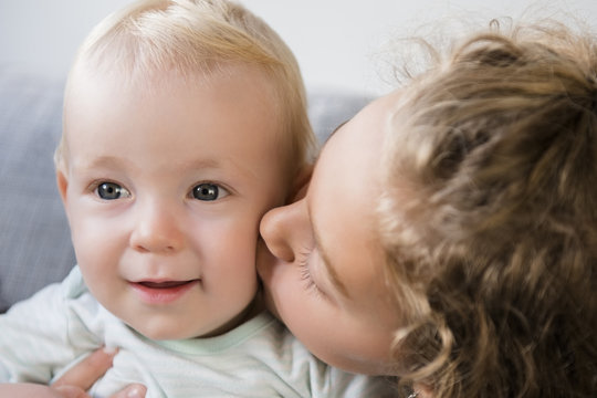 Smiling Caucasian girl kissing baby brother on cheek