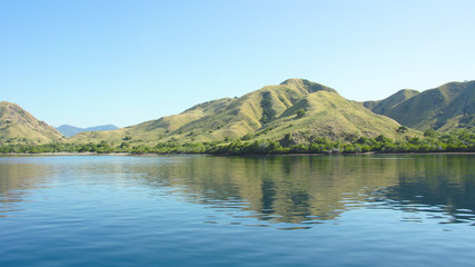 Coastline of mountains with green vegetation reflected  in blue ocean water at Labuan Bajo in Flores, Indonesia.