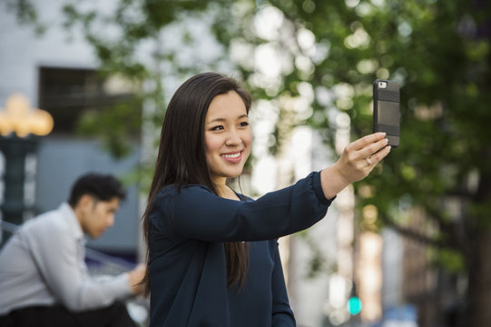 Chinese businesswoman posing for cell phone selfie outdoors