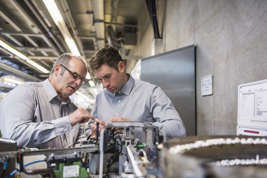 Two men in factory shop floor examining outcome of a machine