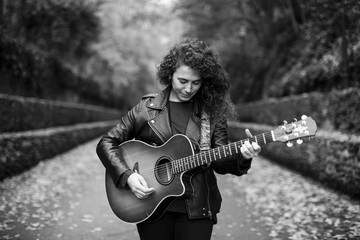 Beautiful young woman playing guitar on forest, fashion lifestyle. Girl wearing black jacket. Image...