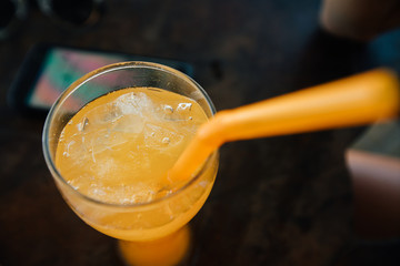 Orange juice with ice and a straw, close-up. A phone and a hand .