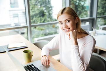 Cheerful lady sitting in office coworking while using laptop