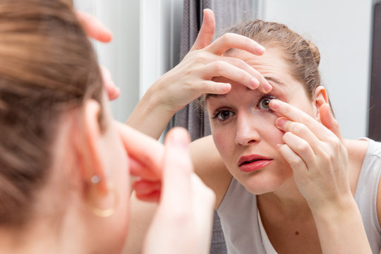 beautiful girl applying or removing a contact lens with mirror