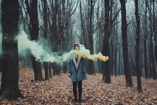 Woman holds up yellow smoke flare to signal for help in the middle of nature