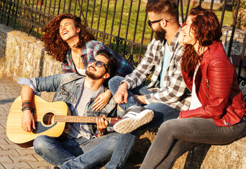 Group of young friends hangout at the city downtown.They singing and playing guitar.