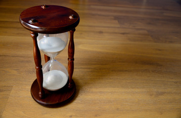 Hourglass, clock in front of wooden background with a copy space. Time is running off. Application date or deadline. Close up.