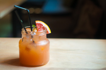 A refreshing summer lemonade with grapefruit. In a glass jar with a straw for drinking. Standing on a wooden table.