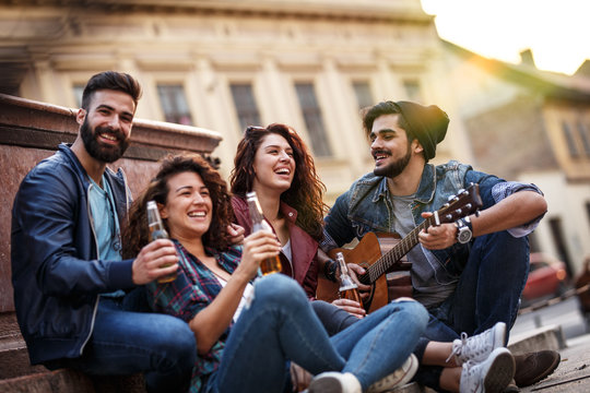 Group of friends  hangout on street in city downtown.They standing by the city square,drinking and playing guitar.