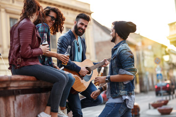 Group of young friends hangout on city square  downtown.They drinking and playing guitar.