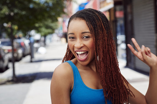 Smiling woman gesturing peace on city sidewalk