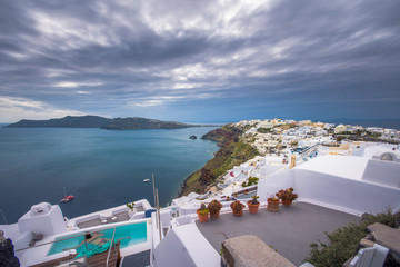 Oia town on Santorini island, Greece. Traditional and famous houses, churches with blue domes over the Caldera, swimming pool,  jacuzzi, Aegean sea